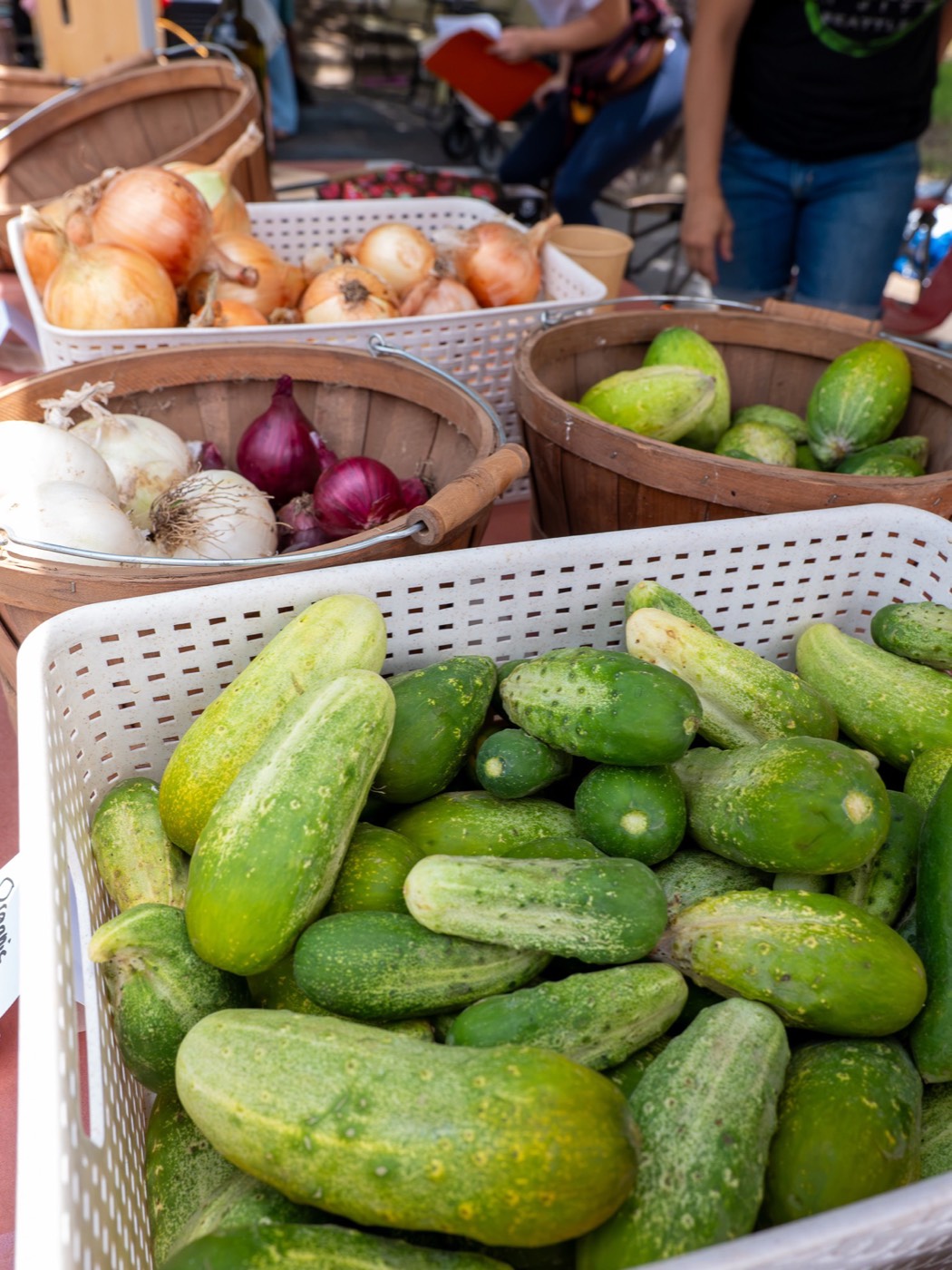 Baskets of cucumbers, white and red onions on a market table