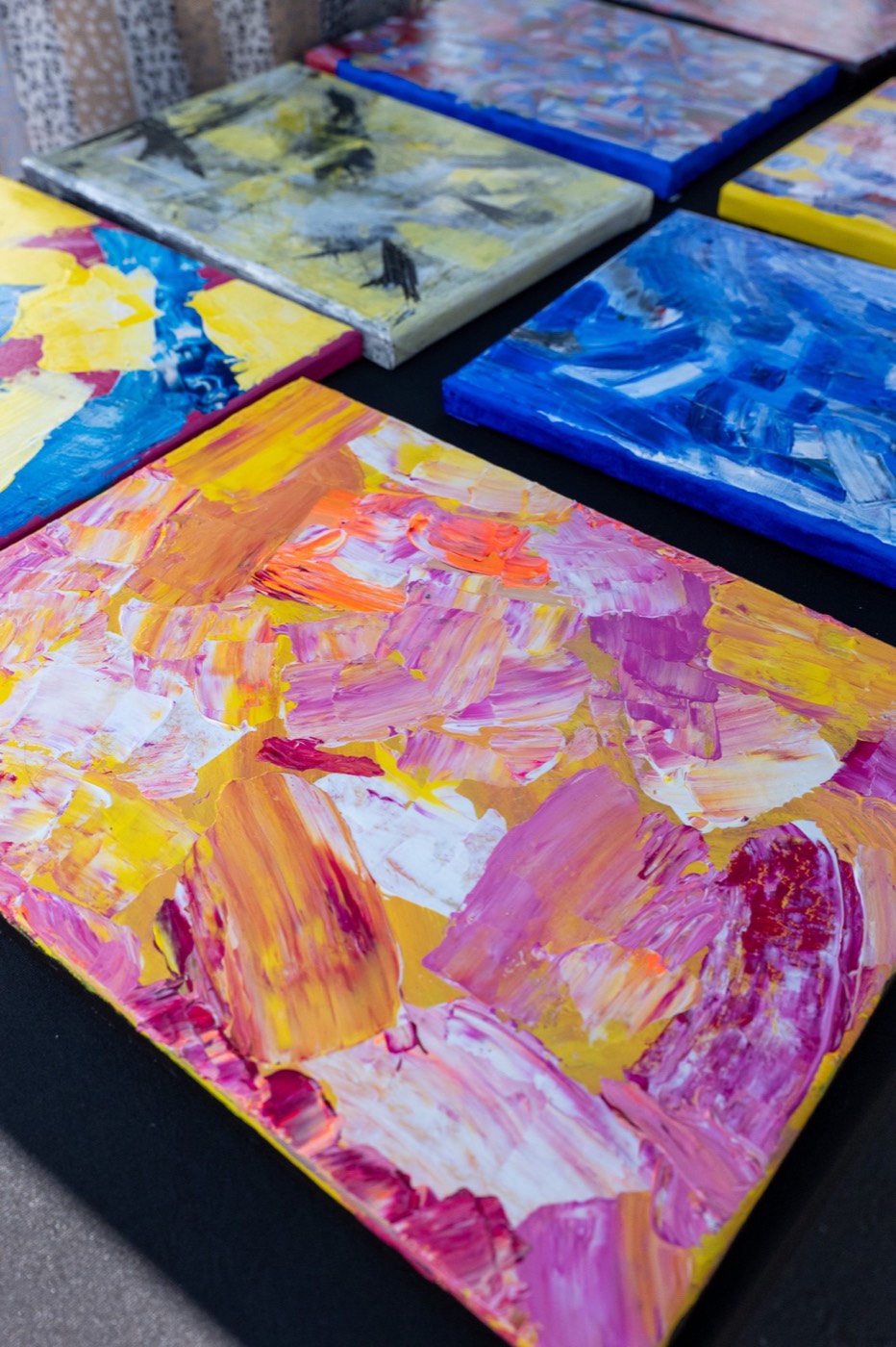 Brightly coloured abstract paintings on canvas laid out on a table