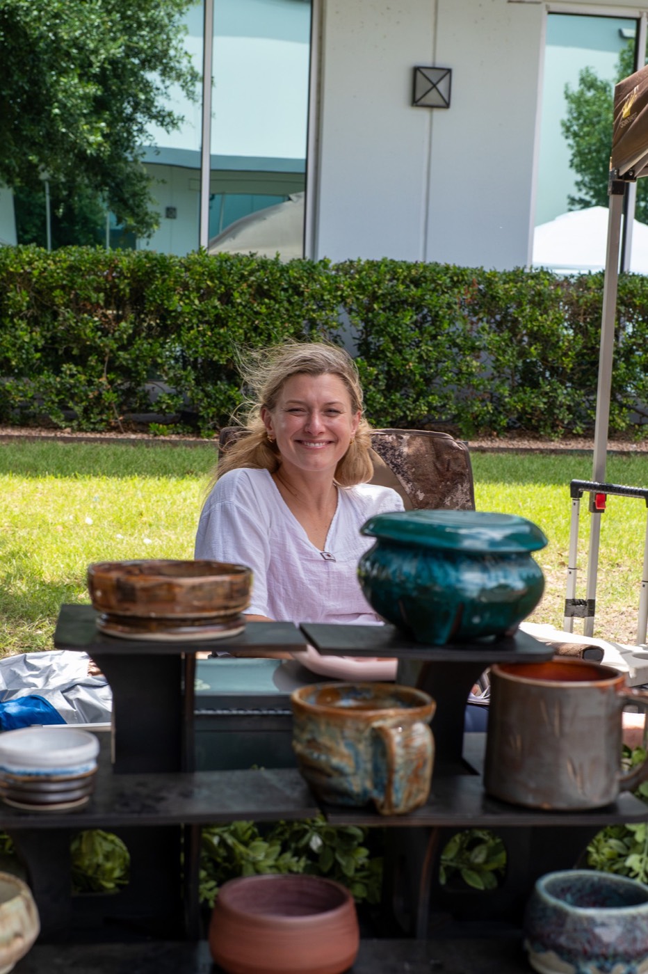A potter sitting behind a stand of handmade glazed bowls and mugs