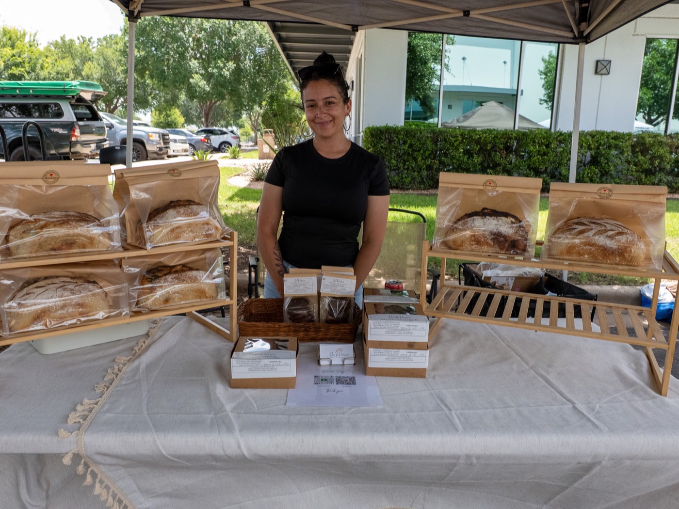 A baker behind a table of bagged sourdough loaves under a canopy